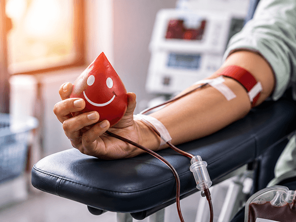 A blood donor holding a smiling blood-drop stress ball during donation
